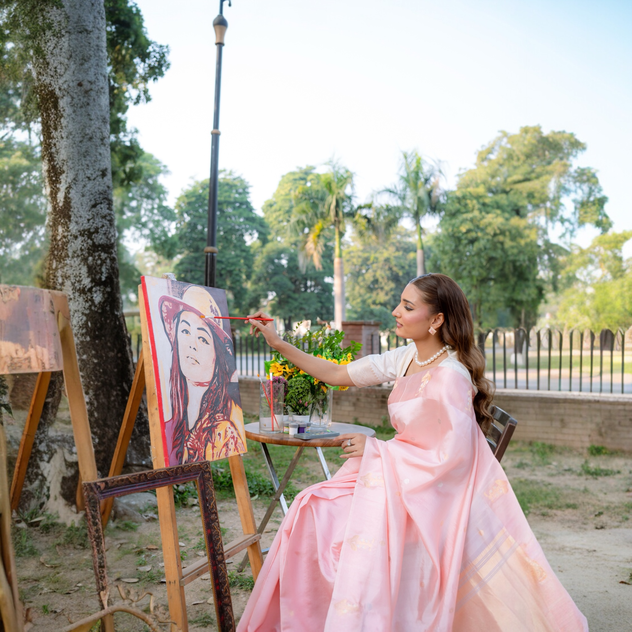 Woman in a pink banarasi saree painting an easel outdoors Lunarae London