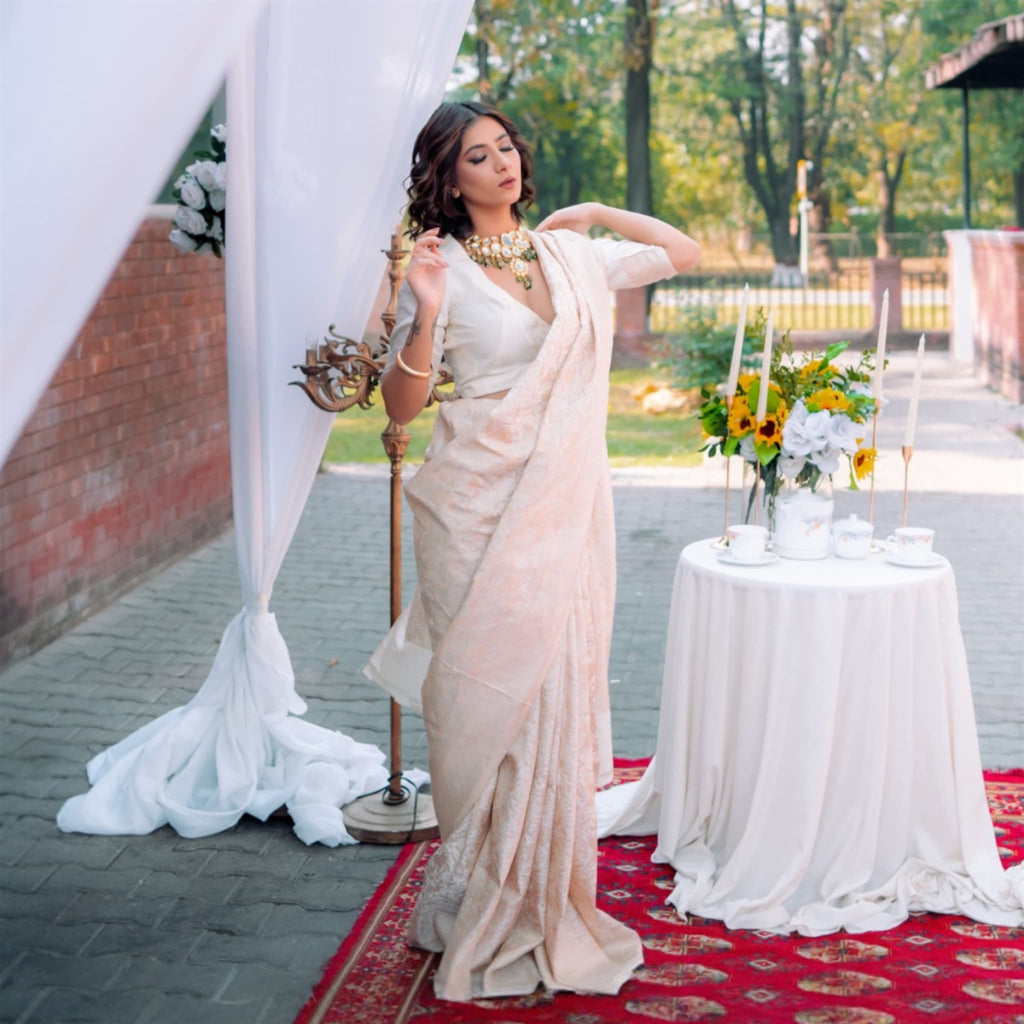 Woman in a white saree standing next to a decorated table outdoors.