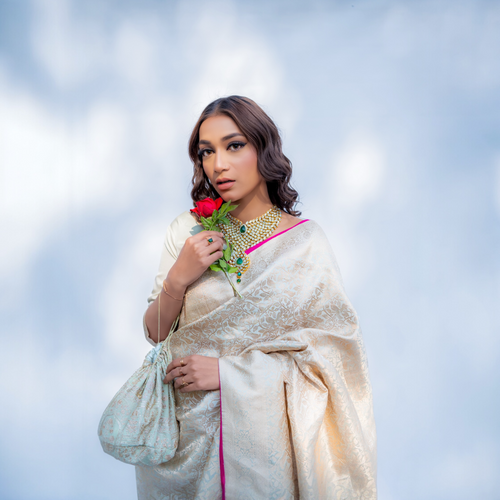 Woman in a Pistachio green Katan silk Banarasi saree with Shikargah motif from Ivory Whisper collection holding flowers against a light blue background